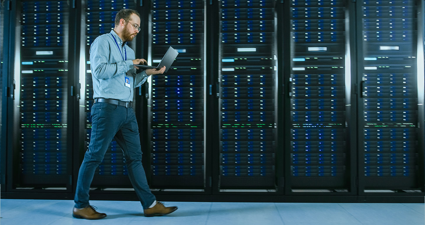 IT professional walks in front of a row of server racks in a data center
